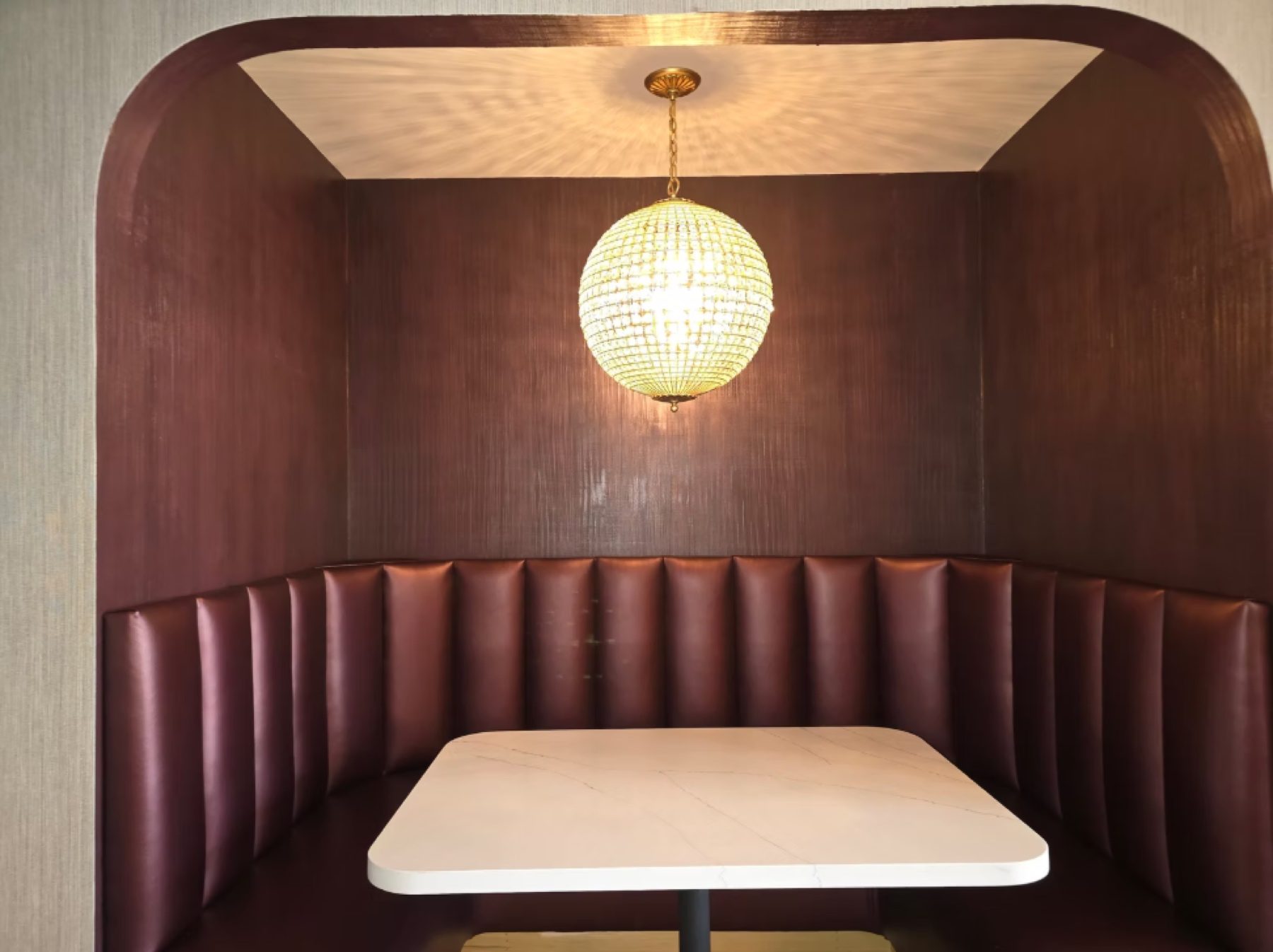 Restaurant booth with hand-finished burgundy walls under a crystal globe pendant