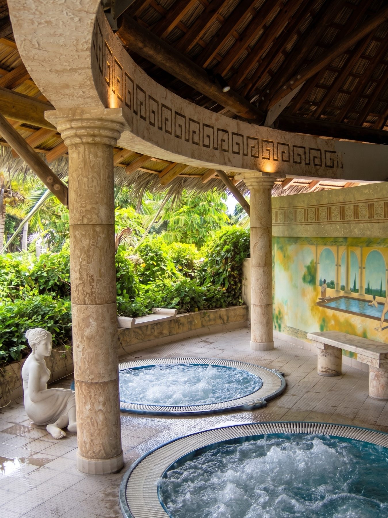 Carved columns and hand-finished surround framing a circular spa under a thatched roof